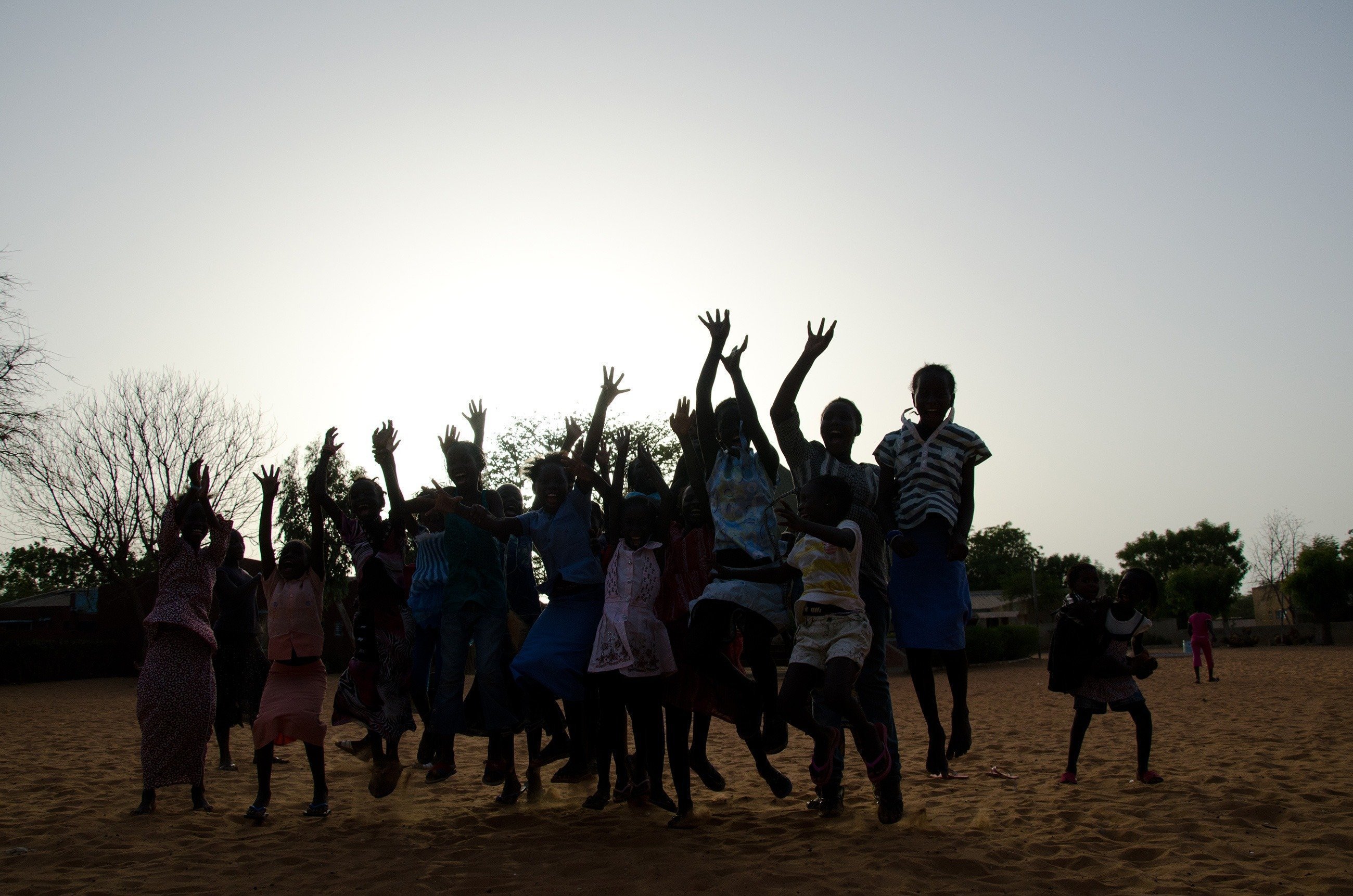 Eine Gruppe von Kindern springt vor einem Sonnenuntergang hoch.