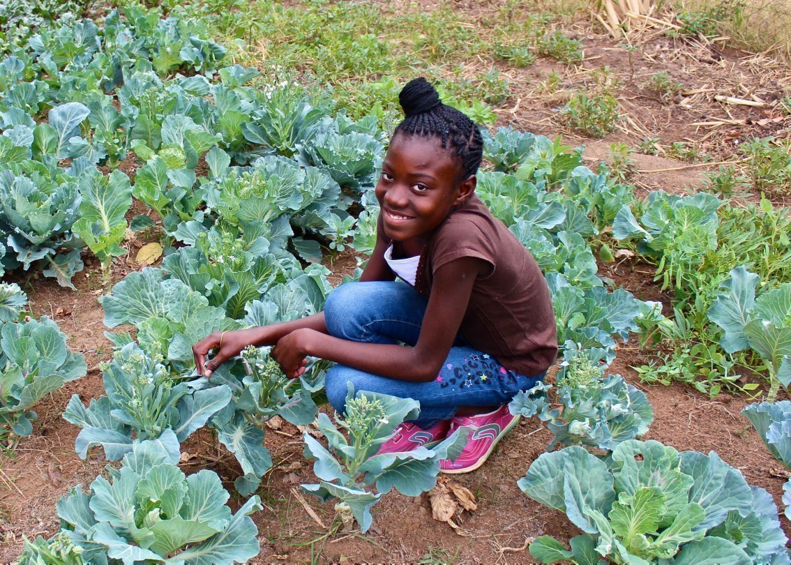 Afrikanisches Kind aus einem SOS-Kinderdorf sitzt im Gemüsebeet und kümmert sich um den Salat.