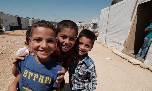 Drei syrische Jungs lächeln sich umarmend in die Kamera.
